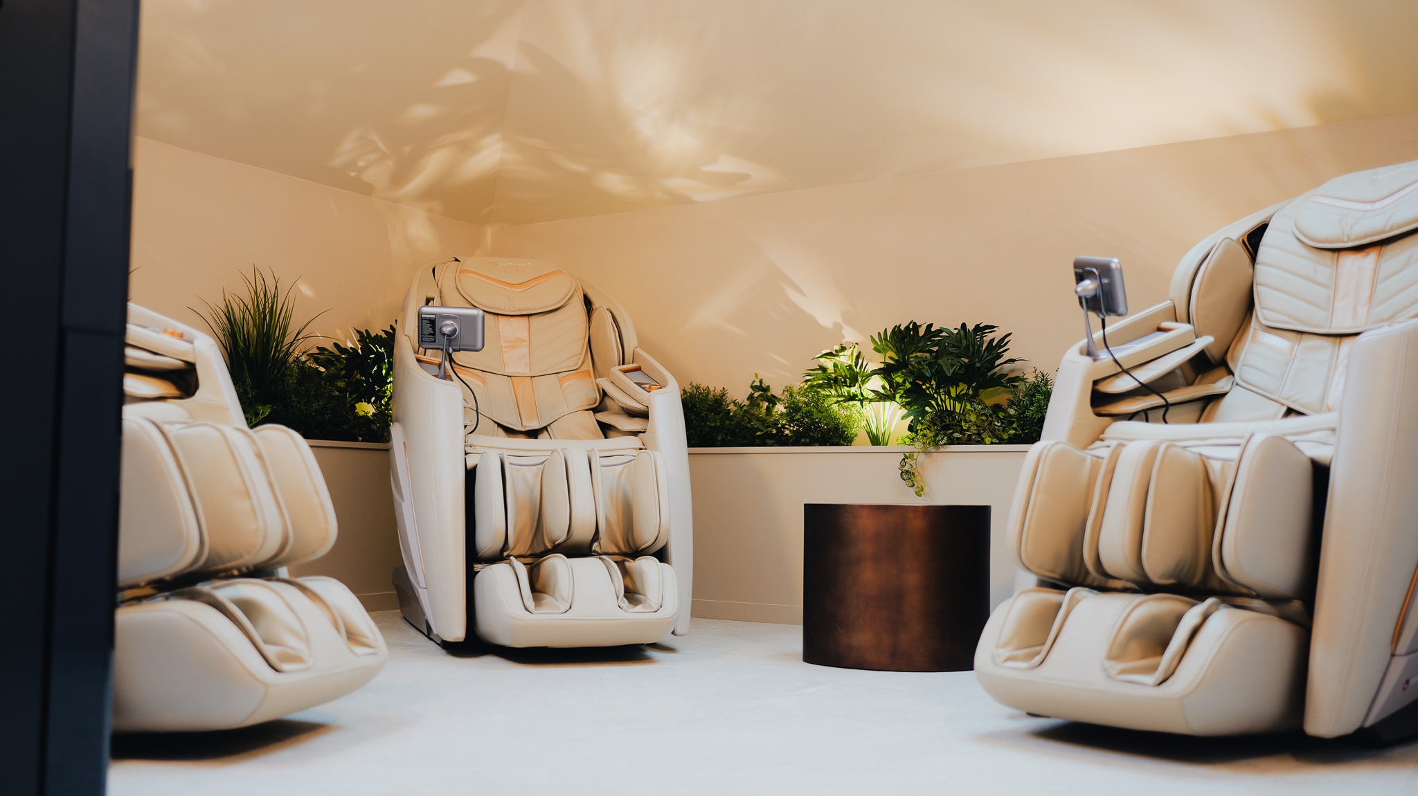 Trois fauteuils de massage beige disposés en cercle avec une table ronde et des plantes vertes en arrière-plan