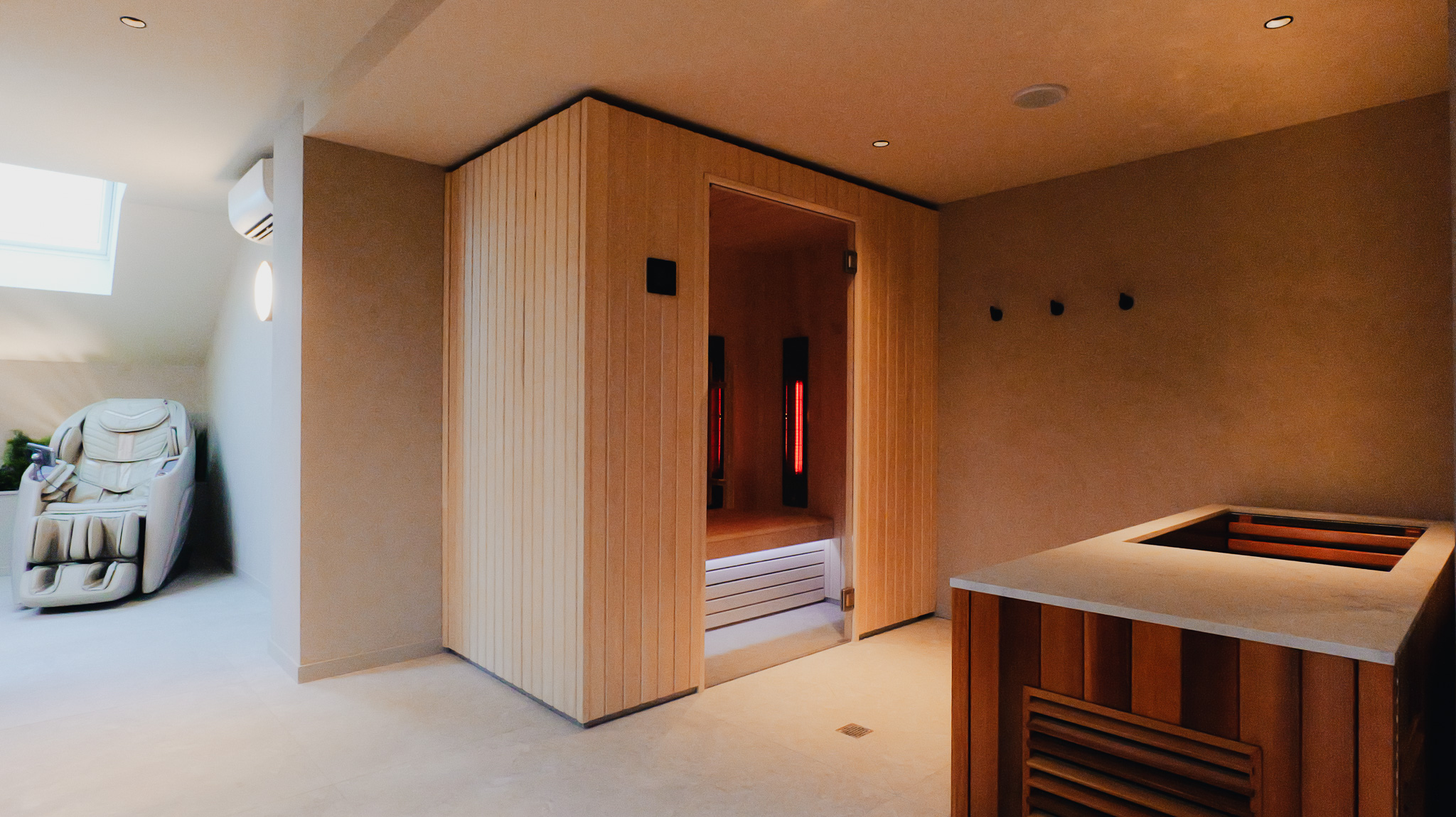 espace spa intérieur avec cabine infrarouge en bois, fauteuil de massage beige et banquette en bois avec comptoir clair